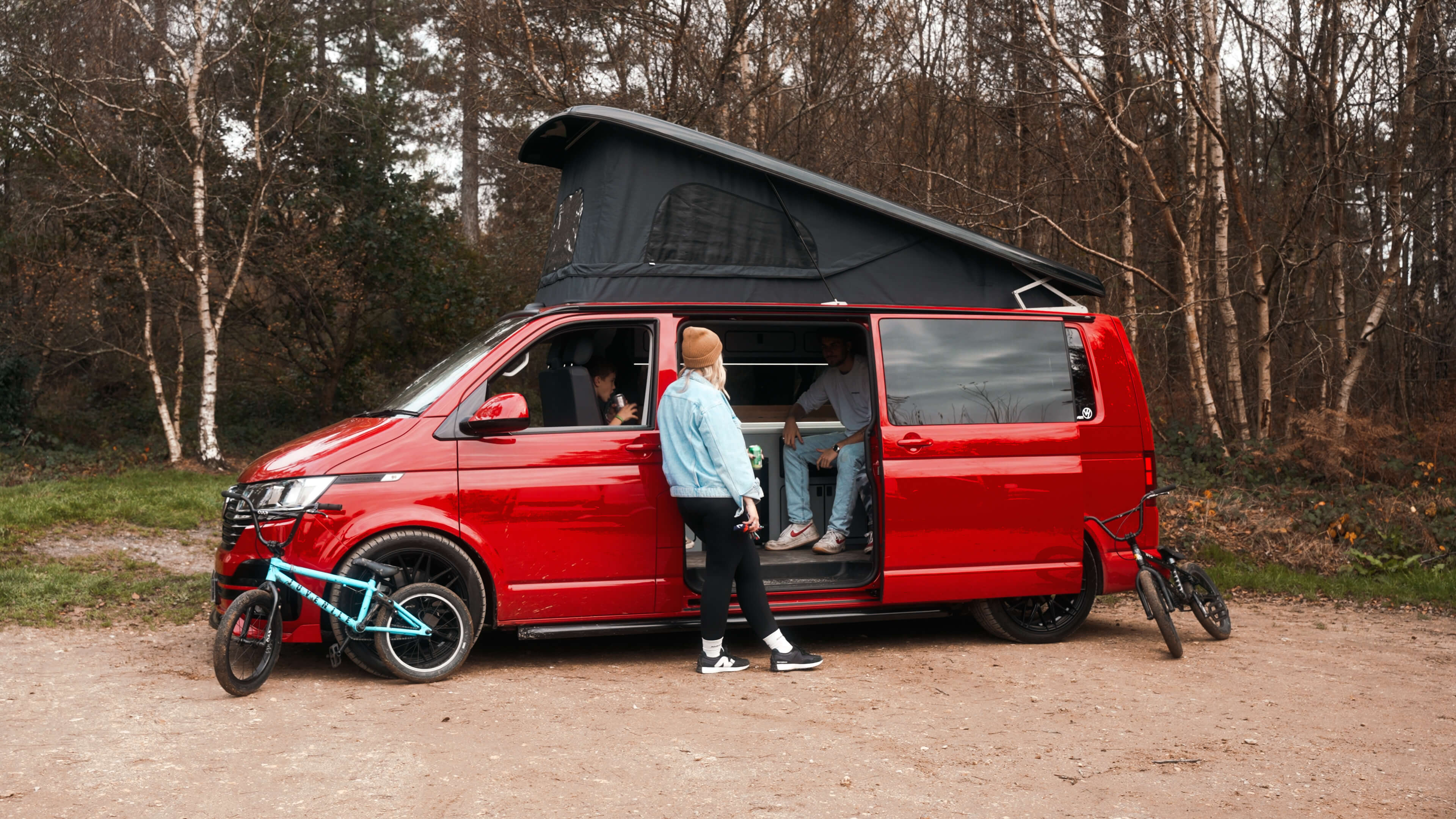 Van Haven camper with pop-top roof raised, family loading bikes in woodland